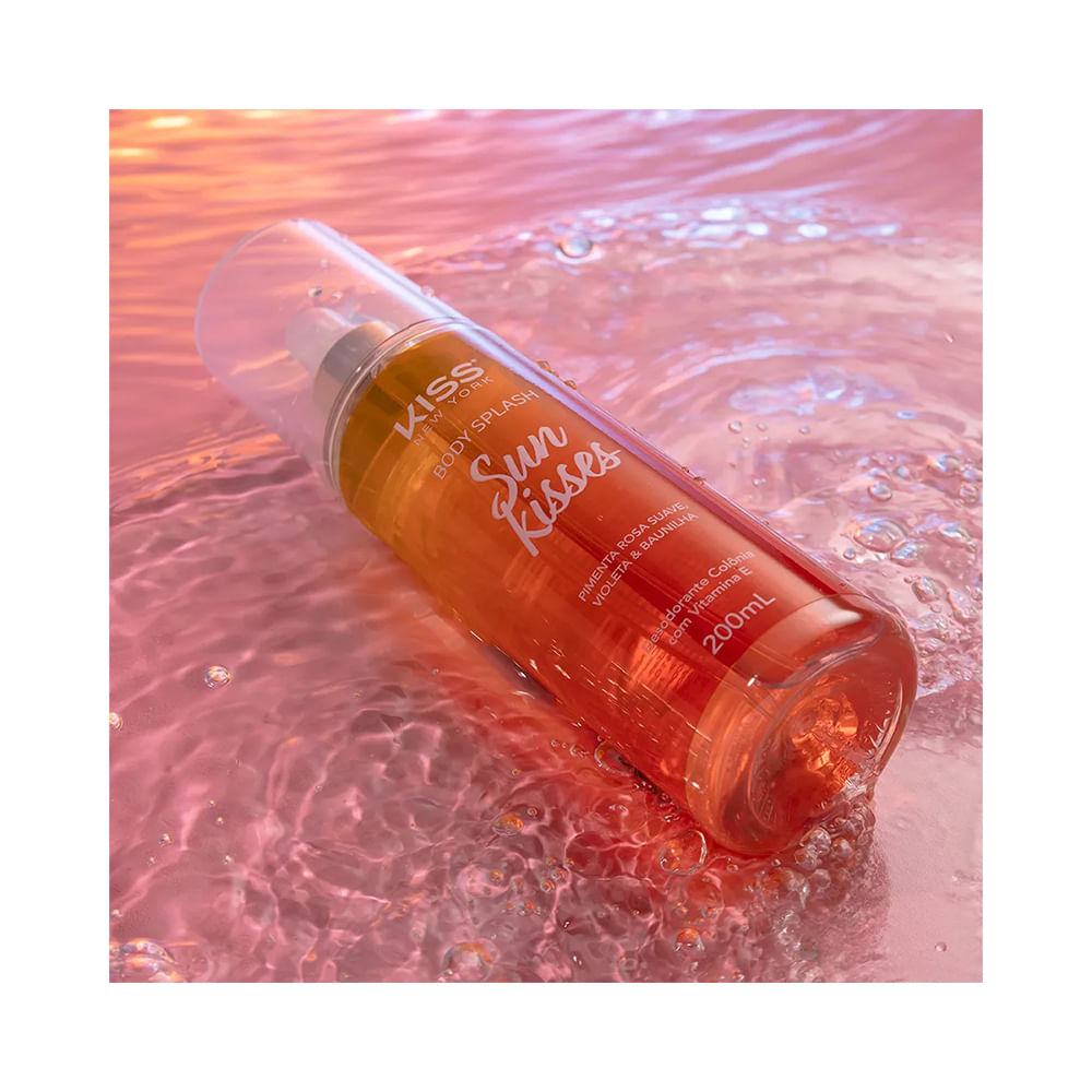 Frasco do Body Splash Kiss New York Sun Kisses 200ml deitado em superfície com água cor de rosa refletindo luz
